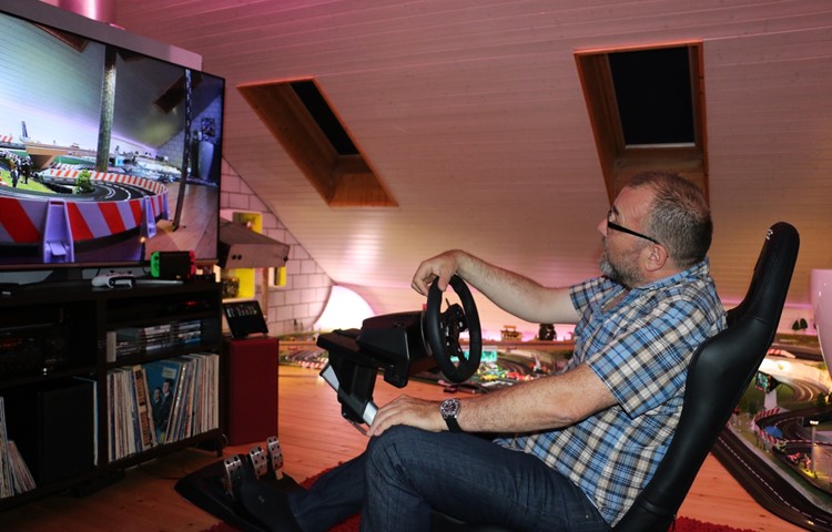 Am Bildschirm lenkt Rolf Eigenheer virtuelle Autos, auf der Carrerabahn dahinter Modellautos im Massstab 1:32.