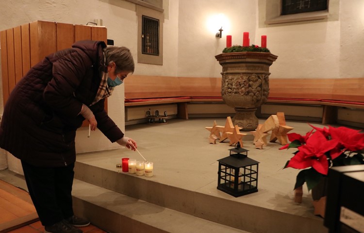 Eine Gottesdienstbesucherin nimmt das Friedenslicht nach Hause. Dieses befindet sich in der schwarzen Laterne (rechts im Bild), und daran kann man seine eigene mitgebrachte Kerze anzünden.