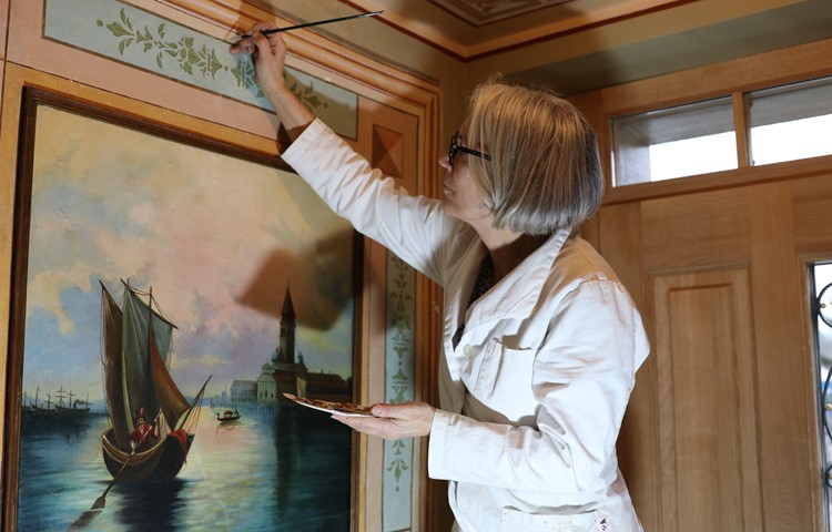 Anita Wanner restauriert die Wandmalerei im Gang der Friedau, im Hintergrund die aufgedoppelte Türe.