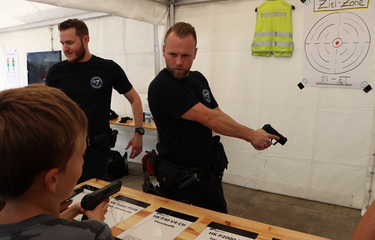 Ein Polizist zeigt einem jungen Besucher, wie die Pistole richtig gehalten wird.