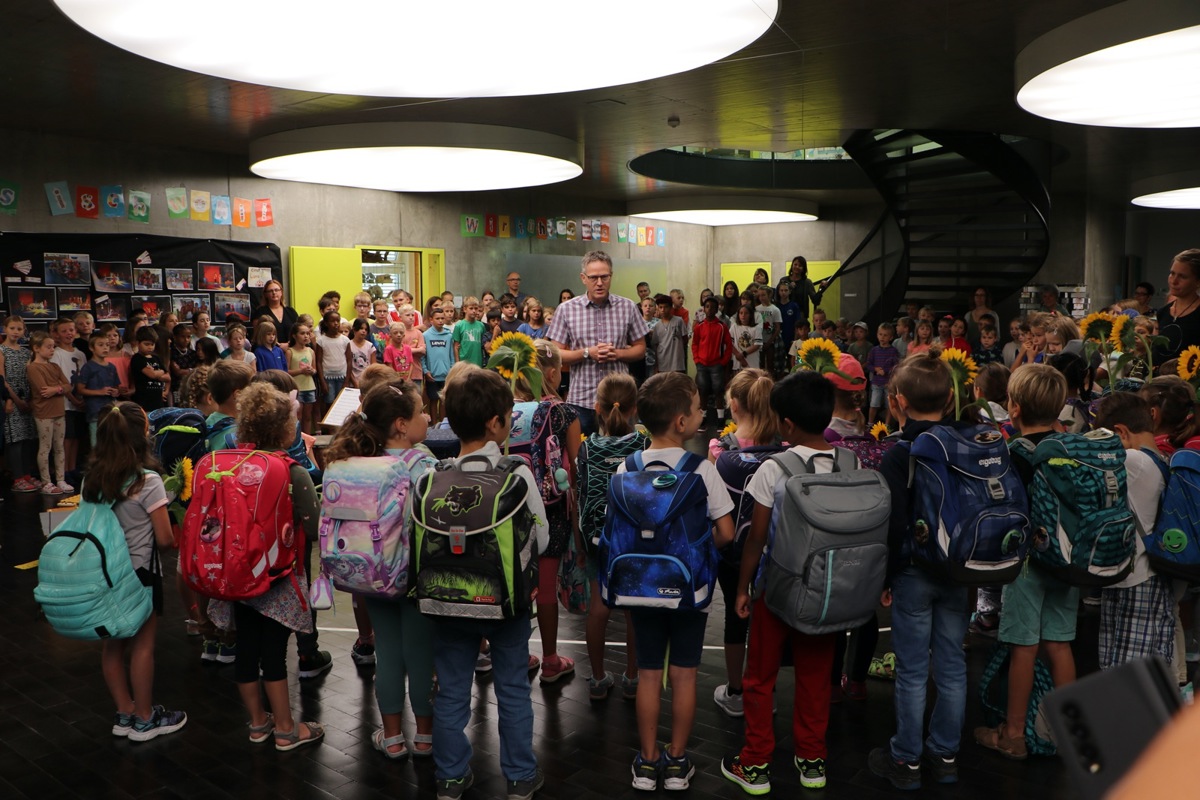 Schulleiter Marius Strebel und die älteren Kinder begrüssen die neuen Erstklässlerinnen und Erstklässler.