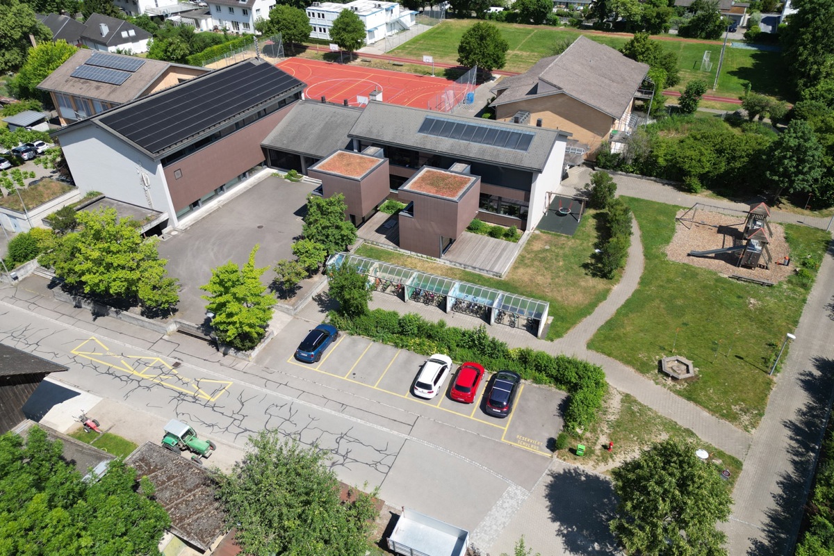 Zurzeit sind beim Schulhaus Zielacker in Kleinandelfingen an fünf Orten 75 Velos abgestellt. Neu werden alle auf dem Blätz mit dem Sandkasten und dem Klettergerüst angeordnet (im Bild rechts, die Bauvisiere stehen). Beim Schulhaus selber bleibt Platz frei für einen möglichen dritten Kubus mit Gruppenräumen. Und Schulbusse halten künftig nicht mehr auf der Strasse.