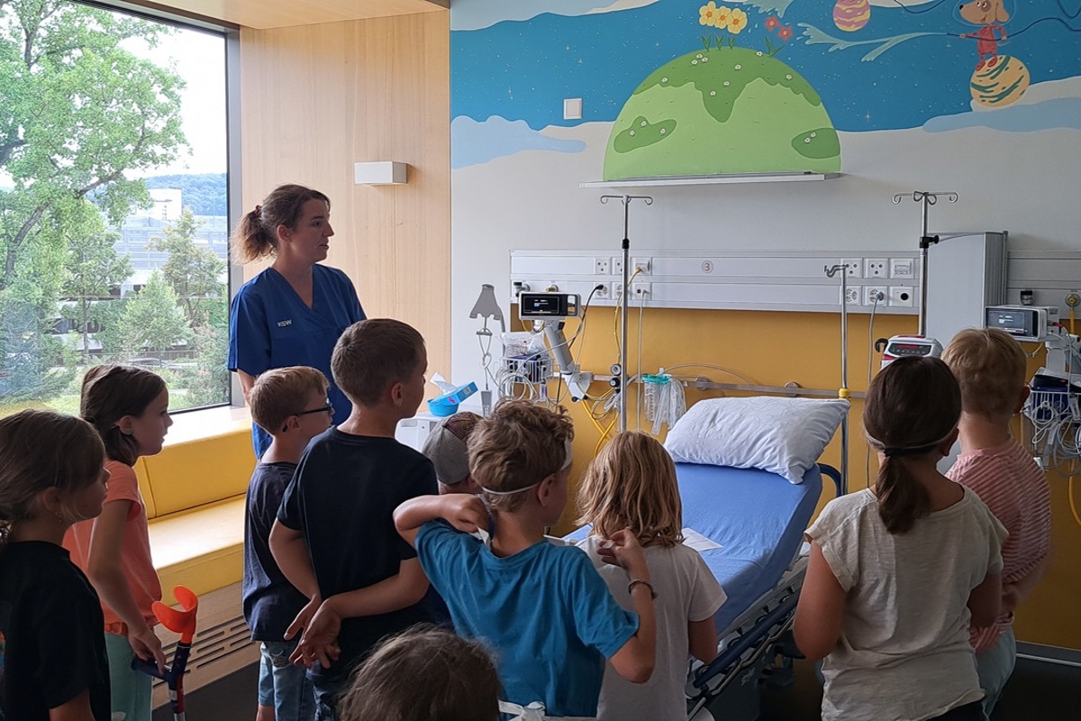 Pflegefachfrau Christa Boulos zeigt den Schülerinnen und Schülern ein Zimmer auf der Kinderstation und erklärt